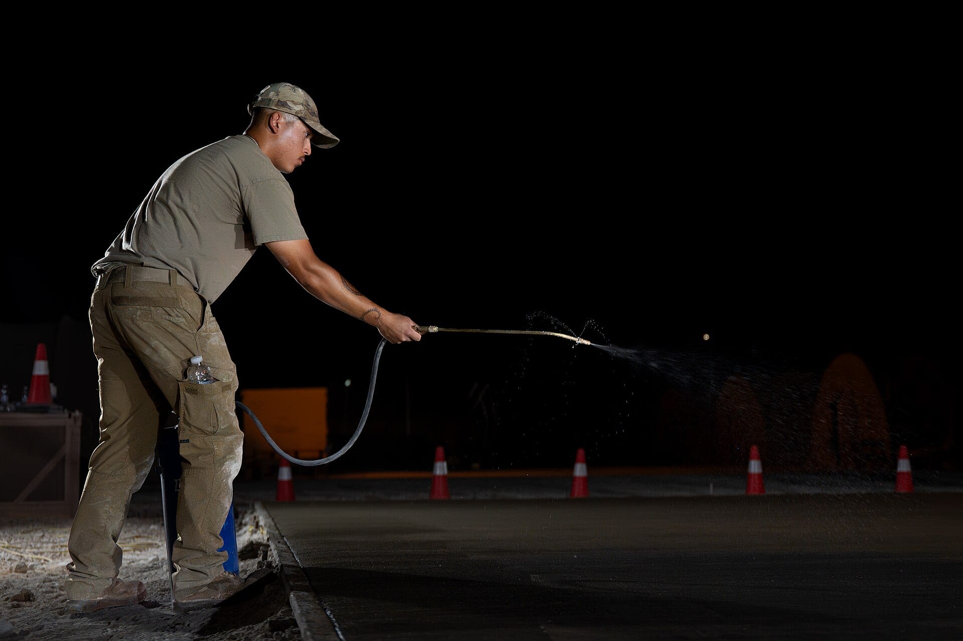 A worker spraying a curing application across a fresh slab at night